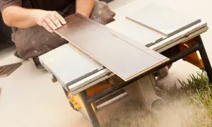 Ręce układają panel na pile stołowej, pokazując, czym ciąć panele. W tle widać kurz.