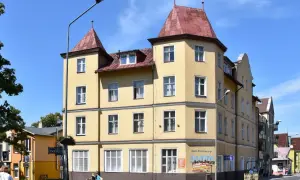 Żółta kamienica w Międzyzdrojach, z banerem "Delfin Międzyzdroje Cennik" i reklamą "Delfin Domowe Obiady".