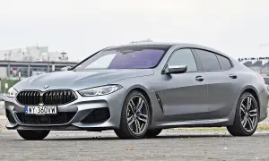 Szary BMW M8 Gran Coupe z czarnym dachem i felgami, zaparkowany na ulicy.