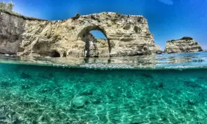 Arco naturale e faraglioni nel mare cristallino del Salento, il mare più bello. Acqua turchese e rocce bianche sotto un cielo azzurro.