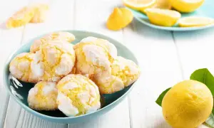 Biscotti al limone, morbidi e profumati, in una ciotola azzurra, con limoni freschi e spicchi su un piattino sullo sfondo.