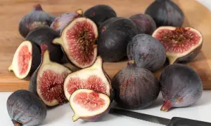 Jak jesc figę? Kilkanaście dojrzałych, ciemnych fig, niektóre przekrojone, ukazujące różowe wnętrze, leży na desce.