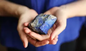Manos sostienen un trozo de lapislázuli, su intenso azul resalta contra la tela azul.