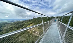 Himmelbrücke in Dolní Morava mit Blick auf bewaldete Hügel und eine Fernsehturm-ähnliche Struktur.