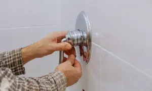 Mani che lavorano per smontare miscelatore doccia a muro.