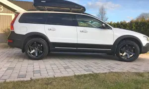 Vit Volvo XC70 2016 med takbox och svarta fälgar. Kanske ett problem med att få plats med allt bagage?