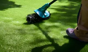 Persona realizando mantenimiento de césped artificial con un cepillo eléctrico.