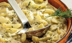 Cremige geschmorte Gurken mit Dill in einer Terrine, serviert mit einer Schöpfkelle.