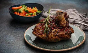 Un savoureux jaret de porc rôti, glacé et parsemé de baies roses, servi avec des légumes vapeur.
