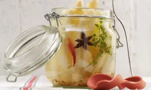 Ein Glas mit eingelegtem Spargel, Gewürzen und Kräutern. Der Deckel ist geöffnet.