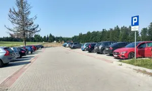 Parking przy górze Jagodnej. Samochody zaparkowane na utwardzonym placu, w tle las i domki.