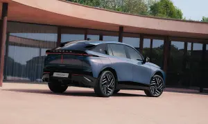 Lancia Gamma 2026, un'elegante berlina blu metallizzato con fari posteriori a LED, parcheggiata davanti a un edificio moderno.