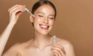 Uśmiechnięta kobieta aplikuje serum z niacynamidem. Dowiedz się, jak stosować niacynamid dla promiennej cery.