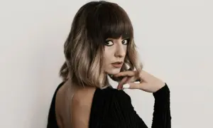 Kobieta z modnym, **blunt bob** w odcieniach brązu i blondu, w czarnej, eleganckiej sukience, z dłonią opartą o podbródek.
