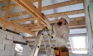 Obrero con casco y martillo realiza refuerzo estructural de vigas de madera en una construcción.