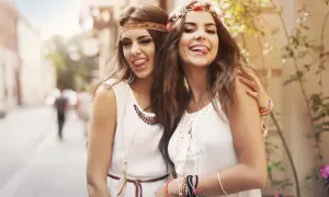 Dwie dziewczyny w styl hippie damski, z kwiatami we włosach, w białych sukienkach, wesoło pokazują języki.
