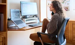 Frau im Homeoffice, die am Schreibtisch sitzt und telefoniert. Das Arbeitszimmer ist gemütlich eingerichtet.