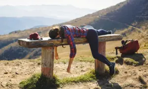Donna esausta si riposa su una panca in montagna, con zaino e cappellino. Ottimi trekking consigli per non finire così!