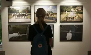 Kobieta ogląda prace na konkursie fotograficznym dla amatorów. Widać krowy na drodze i czarno-białe zdjęcie.