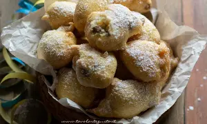 Frittelle di una volta, dolci e soffici, cosparse di zucchero a velo, in un cesto con coriandoli.