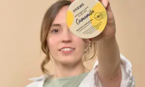 Mujer sonriente sostiene un desmaquillante en crema, "Camomila", que es un sebo limpiador con manteca de karité.