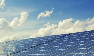 Paneles solares bajo un cielo azul con nubes. El sol brilla, pero la sombra de un posible impuesto al sol en España se cierne sobre la energía renovable.