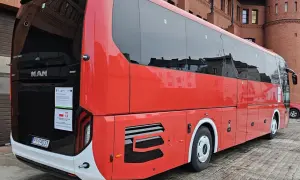 Czerwony autokar MAN Lion's Coach zaparkowany przed ceglanym budynkiem. Może to być przystanek w podróży z Bolesławca do Poznania.