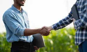 Dwóch mężczyzn ściska sobie dłonie na tle zielonego pola. Jeden z nich, w niebieskiej koszuli, uśmiecha się. To symboliczne potwierdzenie ustnej umowy.