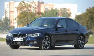 Ciemnoniebieskie BMW 318d z polskimi tablicami rejestracyjnymi stoi na drodze. W tle widać budynki i drzewa.