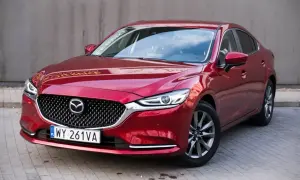 Czerwona Mazda 6 2.0 benzyna z eleganckim grillem i nowoczesnymi światłami, zaparkowana na kostce brukowej.