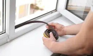 Hände halten eine abgerollte Dichtungsrolle bereit, um die Dichtung zwischen Glas und Rahmen zu erneuern.