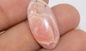 Un óvalo de rodocrosita rosa con vetas blancas, mostrando sus vibrantes propiedades.