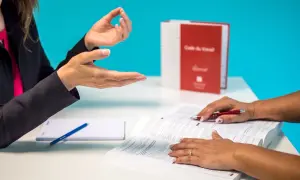 Dwie kobiety rozmawiają przy biurku, jedna wskazuje na otwartą książkę.
