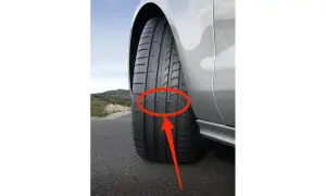 Neumáticos desgastados en un coche plateado en una carretera. La banda de rodadura muestra un desgaste desigual, indicando la necesidad de reemplazo.