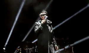 Marilyn Manson na scenie w Warszawie, w czarnym płaszczu i z charakterystycznym makijażem, śpiewa do mikrofonu.