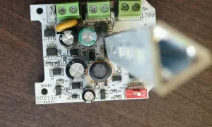 Uszkodzona lampa ostrzegawcza bramy. Widoczny element elektroniczny z okrągłym, czarnym uszkodzeniem.