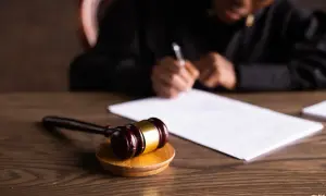 Młotek sędziowski i dokumenty na biurku. Sędzia pisze, finalizując uprawomocnienie wyroku.