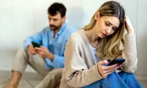 Een vrouw en man zitten apart, beiden op hun telefoon. Ze voelen zich leeg in hun relatie, de afstand tussen hen is voelbaar.