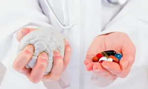 Mains tenant un cerveau en plastique et une poignée de pilules colorées, symbolisant la recherche sur la maladie de Parkinson, dernière découverte.