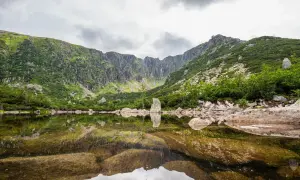 Spokojne, górskie jezioro odbija skaliste zbocza i chmury. Najkrótsza trasa do Śnieżnych Stawków prowadzi przez malowniczy krajobraz.