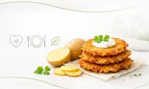 Stos placków ziemniaczanych z kleksem śmietany i natką pietruszki, obok ziemniaków. Zastanawiasz się nad placek ziemniaczany kcal?