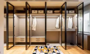 Armario empotrado moderno con puertas de cristal, perchas con ropa blanca y cajones.