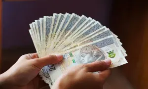 Dłonie trzymają wachlarz banknotów 200 zł. Pieniądze symbolizują świadczenie wspierające, które trafi do potrzebujących.