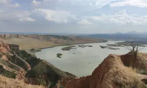 Paisaje de barrancos ocres y un lago sereno, ideal para una ruta de senderismo.
