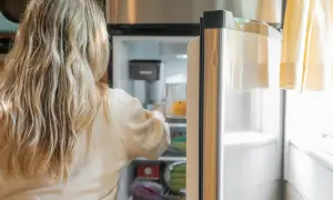 Blondynka wkłada pomarańczę do szuflady nowej lodówki no frost.