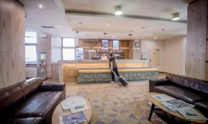 Recepcja hotelu Diament Wisła. Gość z walizką przy ladzie. W holu wygodne kanapy i stoliki z prasą.