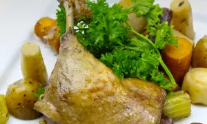 Une savoureuse cuisse de canard confite, accompagnée de pommes de terre et de carottes rôties, garnie de persil frais.