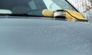 Krople wody na masce samochodu, obok gąbka i słoiczek z woskiem o zapachu miodu.