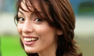Close-up of a young woman with brown hair, smiling and looking to the side.