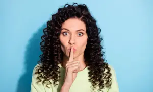 Vrouw met krullend haar houdt vinger voor de mond. Ze zegt niets, want verzwijgen is liegen.